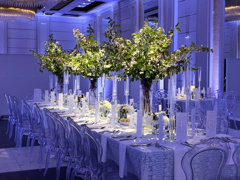 Long candlelit tables in a hall washed in blue and purple uplighting